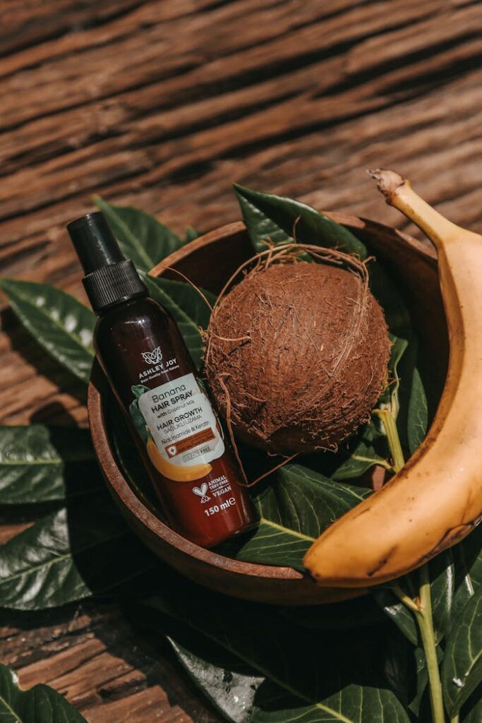 Natural hair spray bottle with banana and coconut arrangement, showcasing organic product on rustic wood.